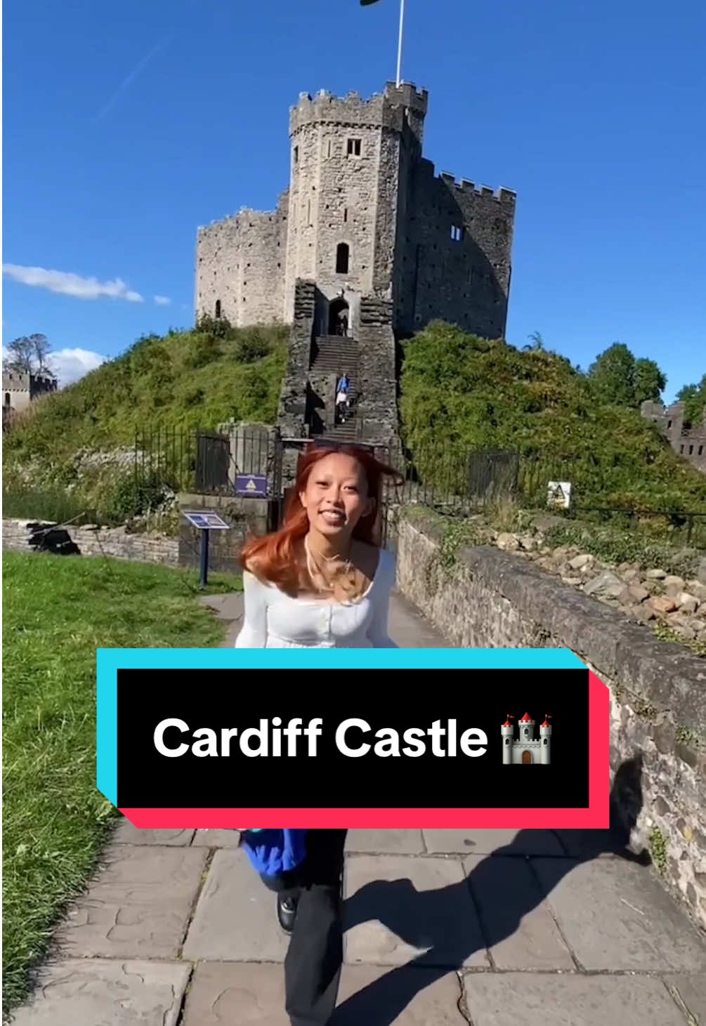 A young woman smiles at the camera while walking through the grounds of Cardiff Castle