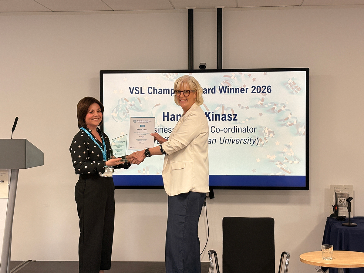 Hannah Kinasz receiving an award from a colleague in front of large monitor