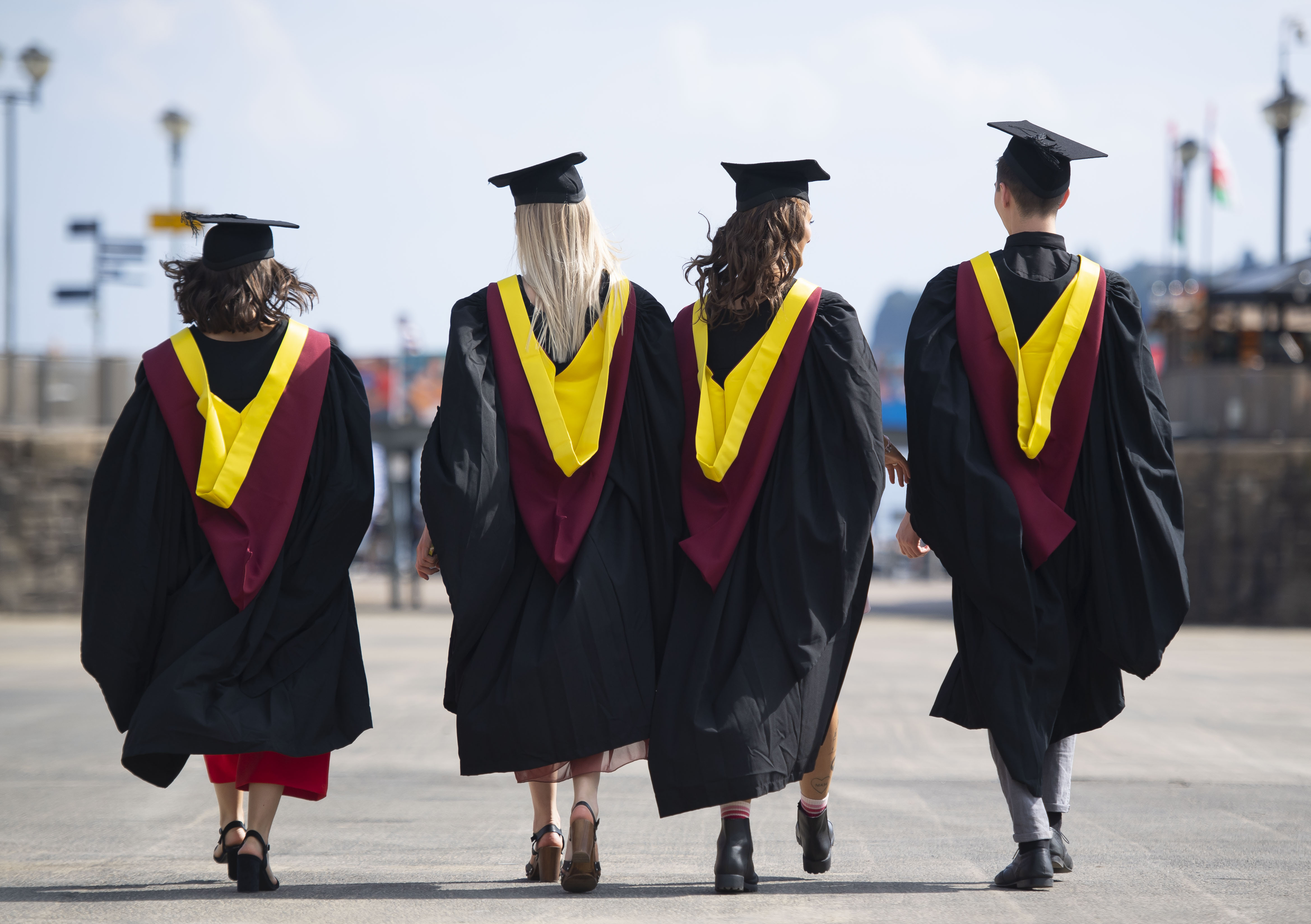 Four students in graduation robes walking away from the camera