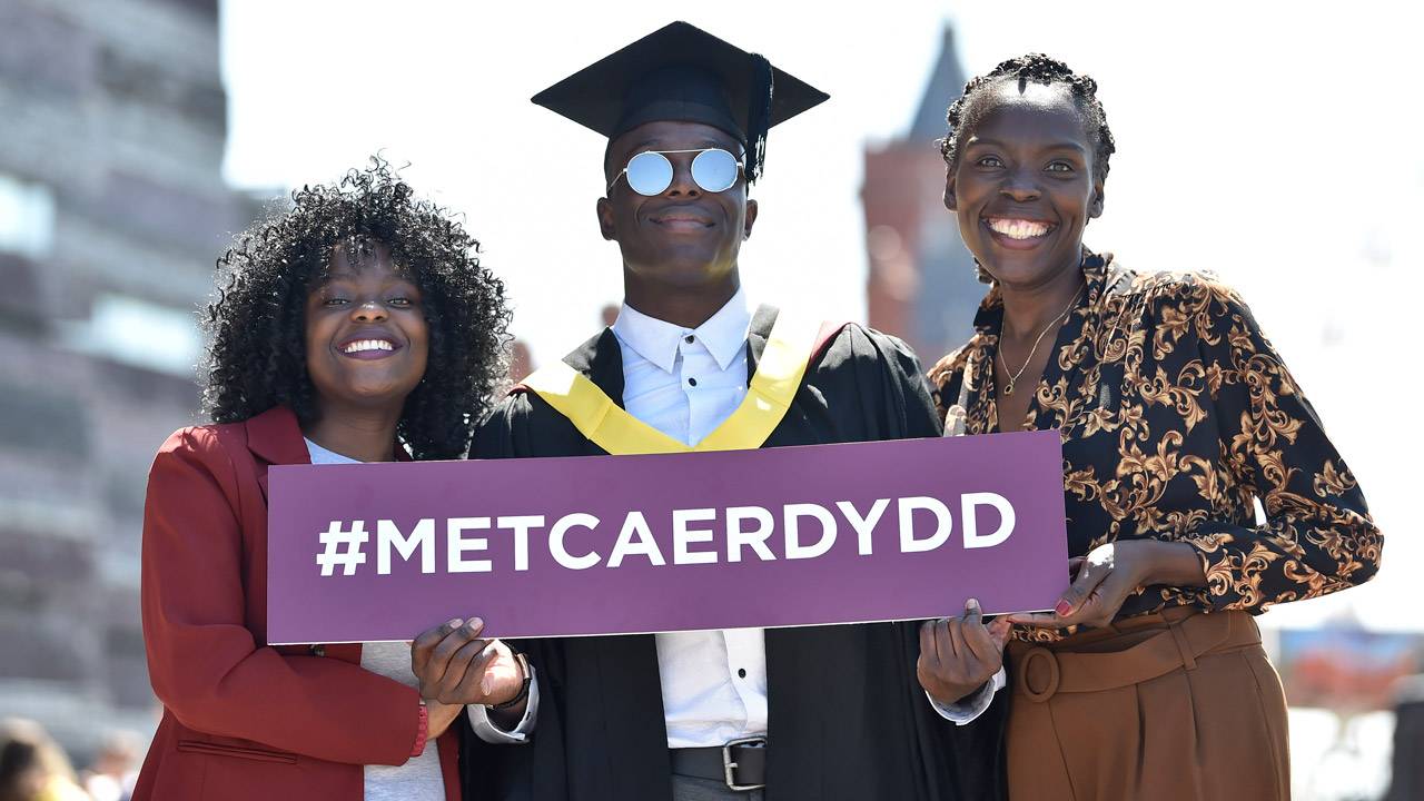 Graduation student with family holding Welsh hashtag sign